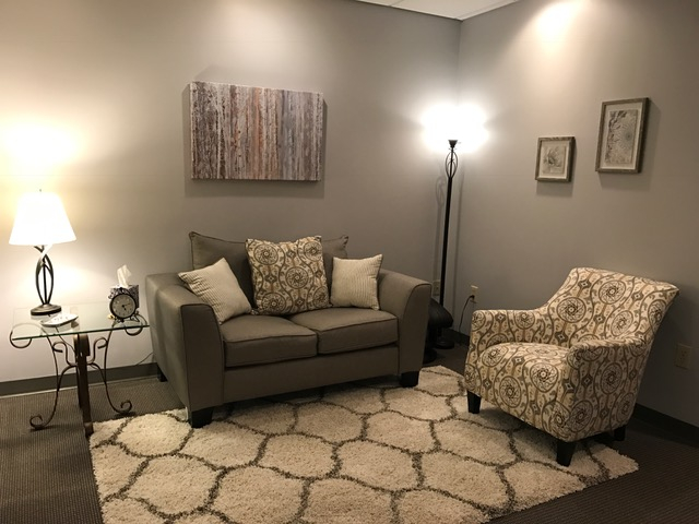 interior shot of office. grey cushioned couch, white patterned cushioned chair and two lamps